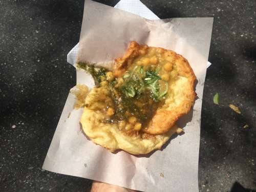 A photo of a hand holding a plate of UWI Doubles