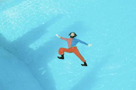 Photograph of Thor Rixon in an orange and blue long sleeve shirt and bright organge pants floating in a bright blue pool